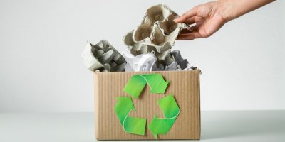 Záběr na krabici s recyklačním symbolem a ruka, která do ní dává prázdná plata od vajíček