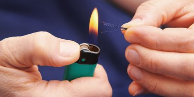 Ruka drží zapalovač s hořícím plamenem u kontrolního vlákna testované látky