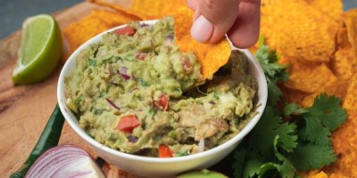 Člověk namáčí nachos do guacamole