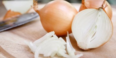 Celá cibule i její plátky na dřevěném prkénku.