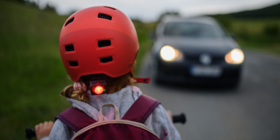 Dítě se světlem na kole v popředí, v pozadí jedoucí auto