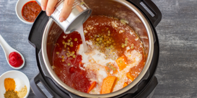 Ruka vlévá do tlakového hrnce s vařící se kari omáčkou mléko