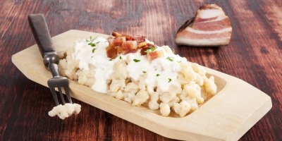 Brynzové halušky na dřevěném talíři ozdobené slaninou