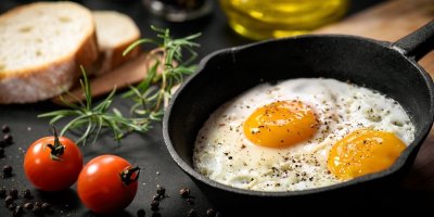 2 sázená vejce v malé černé pánvi, vedle pánve cherry rajčátka a rozmarýn