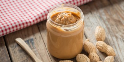 Sklenice arašídového másla s arašídy okolo