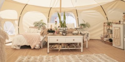 Glampingový stan vybavený pohodlnou postelí a dalším nábytkem, nechybí ani koberec