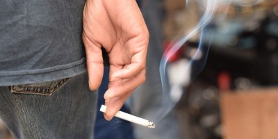 Kouřící cigarety v ruce splývající u nohy