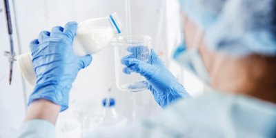 Ruce s modrými rukavicemi nalévají mléko do odměrky