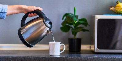 Žena přelévá vodu z varné konvice do porcelánového hrnku