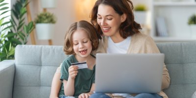Žena s dítětem sedí na gauči s notebookem a platební kartou
