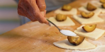 Několik kousků kynutého těsta, na kterém jsou položené kousky švestek