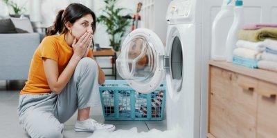 Žena se vyděšeně dívá do pračky, ze které se valí pěna
