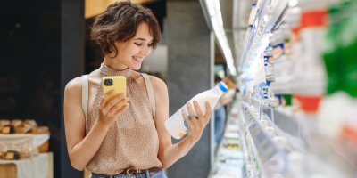 Žena s mobilem v ruce čte etiketu na mléku