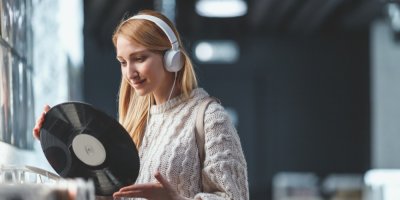 Žena se sluchátky drží v ruce vinylovou desku
