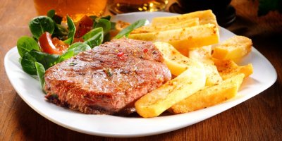 Grilovaný steak se steakovými hranolky, servírovaný na bílém talíři