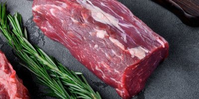 Kus hovězího masa na černém prkénku, kolem snítky rozmarýnu