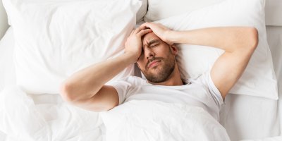 Muž se chytá za bolavou hlavu v posteli