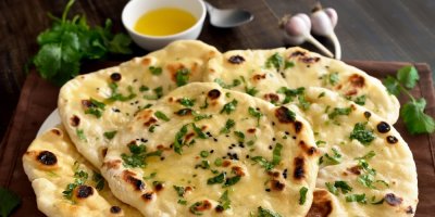 Několik chlebů naan, naskládaných na sobě, jsou přelité máslem a ozdobené koriandrem