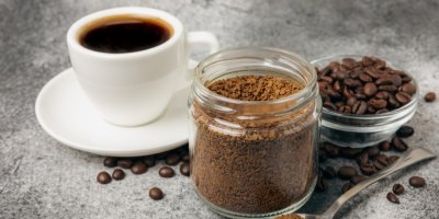 Uvařená káva v hrníčku, sypaná ve skleničce, okolo kávová zrna