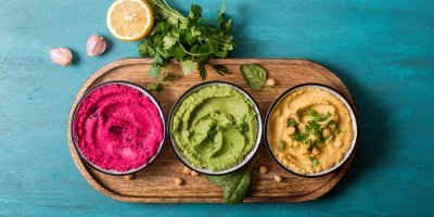 Tři misky s hummusem, červeným, zeleným a béžovým, na prkýnku