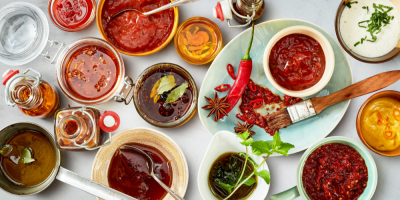 Několik bílých misek se sortimentem jasně červených marinád vedle talířů s bylinkami a dalšími ingrediencemi