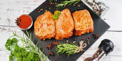 Tři kusy kuřecích stehen marinovaných v červené omáčce na kuchyňském prkénku