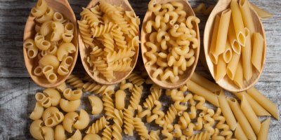 Různé směsi těstovin na dřevěném rustikálním pozadí, pytli a dřevěných lžících