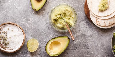 Miska s guacamole, vedle ní rozpůlené avokádo, miska se solí a tortilly