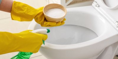 Ruce v rukavicích čistí záchod jedlou sodou a sprejem