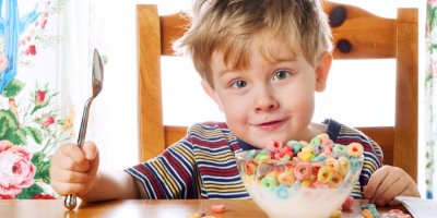 Chlapec sedí u stolu a před sebou má plnou misku barevných cereálií s mlékem