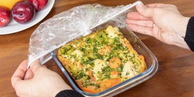 Žena přetahuje průhlednou koupací čepici přes mísu se zapečenou zeleninou