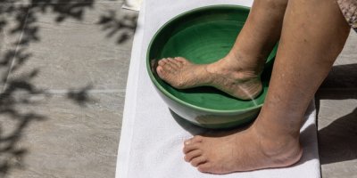 Starší žena si namáčí nohu v lavoru s vodou a solí