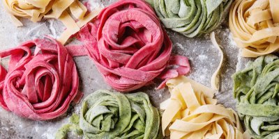 Klubka růžových, zelených a žlutých těstovin na pomoučeném vále