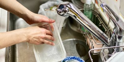 Ruce umývají plastovou krabičku ve dřezu.