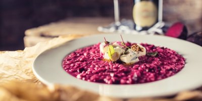 Červené rizoto posypané kousky gorgonzoly a servírované na plochém talíři