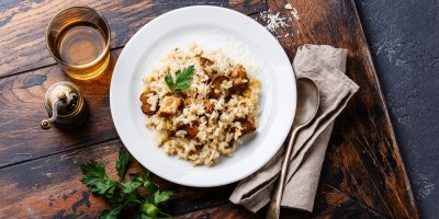 Rizoto s houbami servírované na dřevěném stole ozdobeném snítkou libečku a mlýnkem na koření