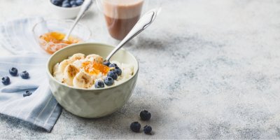 Mléčná rýže v misce se lžící, ozdobená borůvkami, banánem a ovocným rozvarem