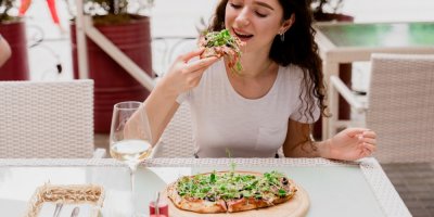 Mladá žena jí kousek pinsy ozdobený zelenými bylinkami