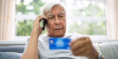 Starší muž telefonuje a přitom si prohlíží svou platební kartu.