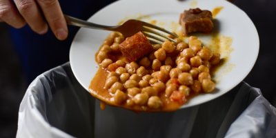 Muž shrnuje vidličkou do koše uvařené jídlo z talíře