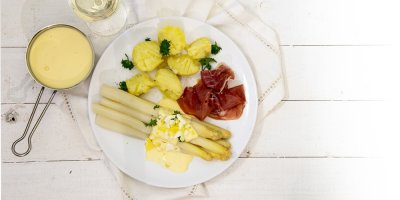 Chřest s brambory a šunkou zalitý béžovou omáčkou na bílém talíři