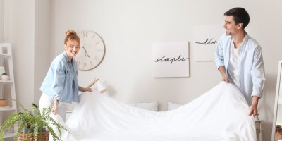 Muž se ženou mění povlečení, oba se u toho usmívají