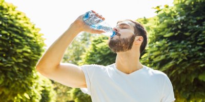 Vousatý muž pije minerální vodu z plastové lahvičky.