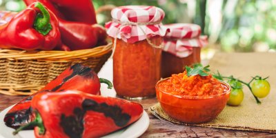 Pečené i čerstvé papriky, ajvar v misce a ve sklenicích