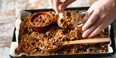 Granola na plechu, v němž je položená dřevěná lžíce a malá miska