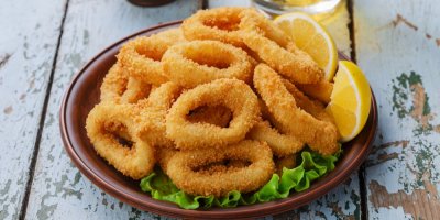 Cibulové kroužky na hnědém talíři se salátem a citronem