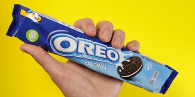 Ruka drží balíček sušenek Oreo na žlutém pozadí