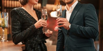 Žena ve třpytivých šatech mluví s mužem, drží v ruce drink