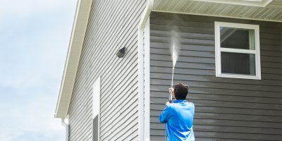 Muž vapkou čistí dům zvenku