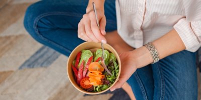 Sedící žena drží v rukou papírovou krabičku se zeleninovým jídlem.